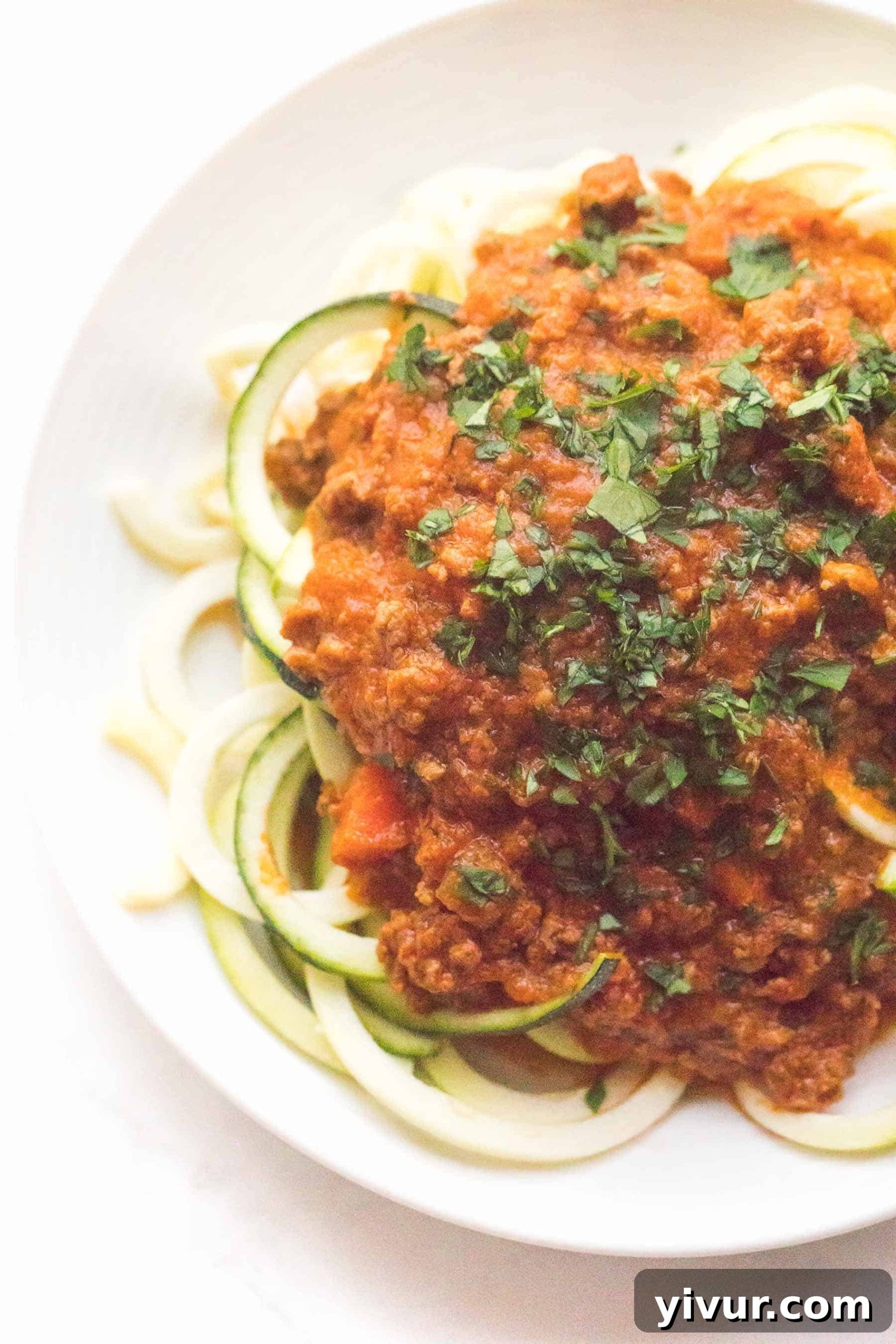 Zucchini noodles with red bolognese sauce on a white plate and background