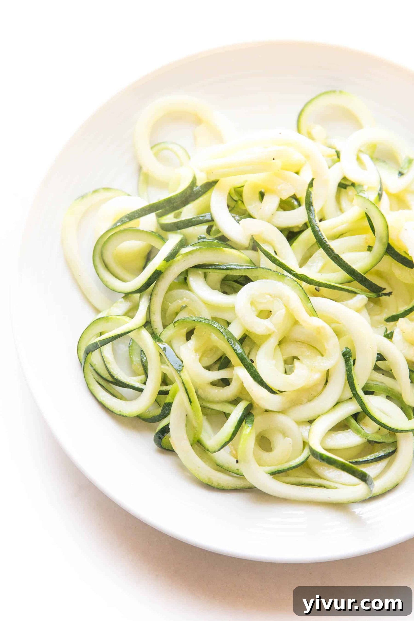 Flavorful Whole30 Keto Zucchini Noodles 2 Freshly spiralized zucchini noodles elegantly arranged on a white plate, showcasing their vibrant green color and readiness for preparation.