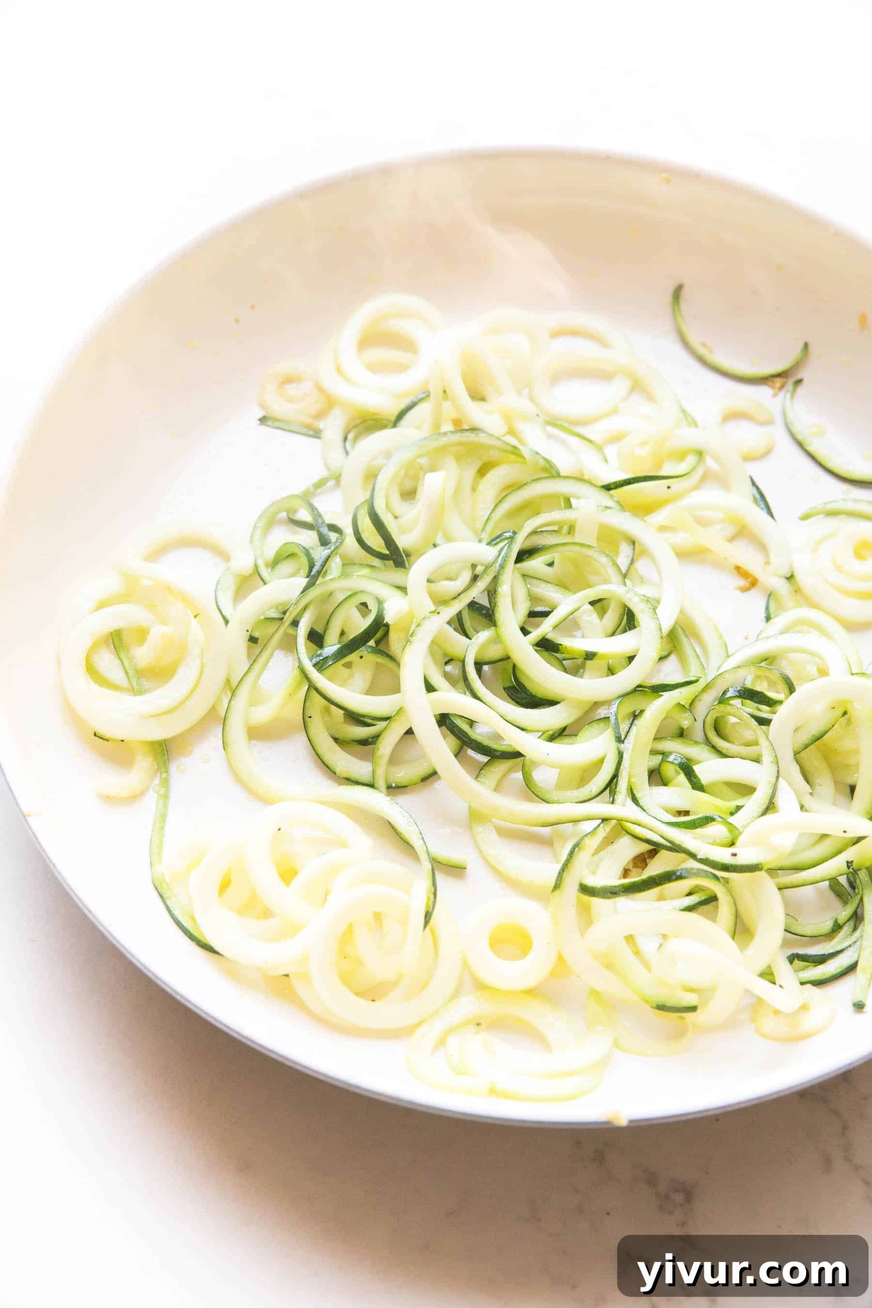 Flavorful Whole30 Keto Zucchini Noodles 3 Firm zucchini noodles being lightly sautéed in a white pan, indicating proper moisture removal for a perfect texture.