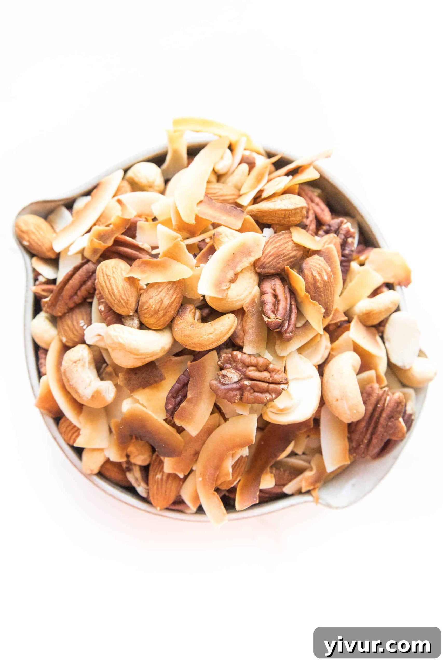 Delicious Whole30 and Keto nuts and coconut chips trail mix in a rustic bowl on a white background, perfect for healthy snacking.