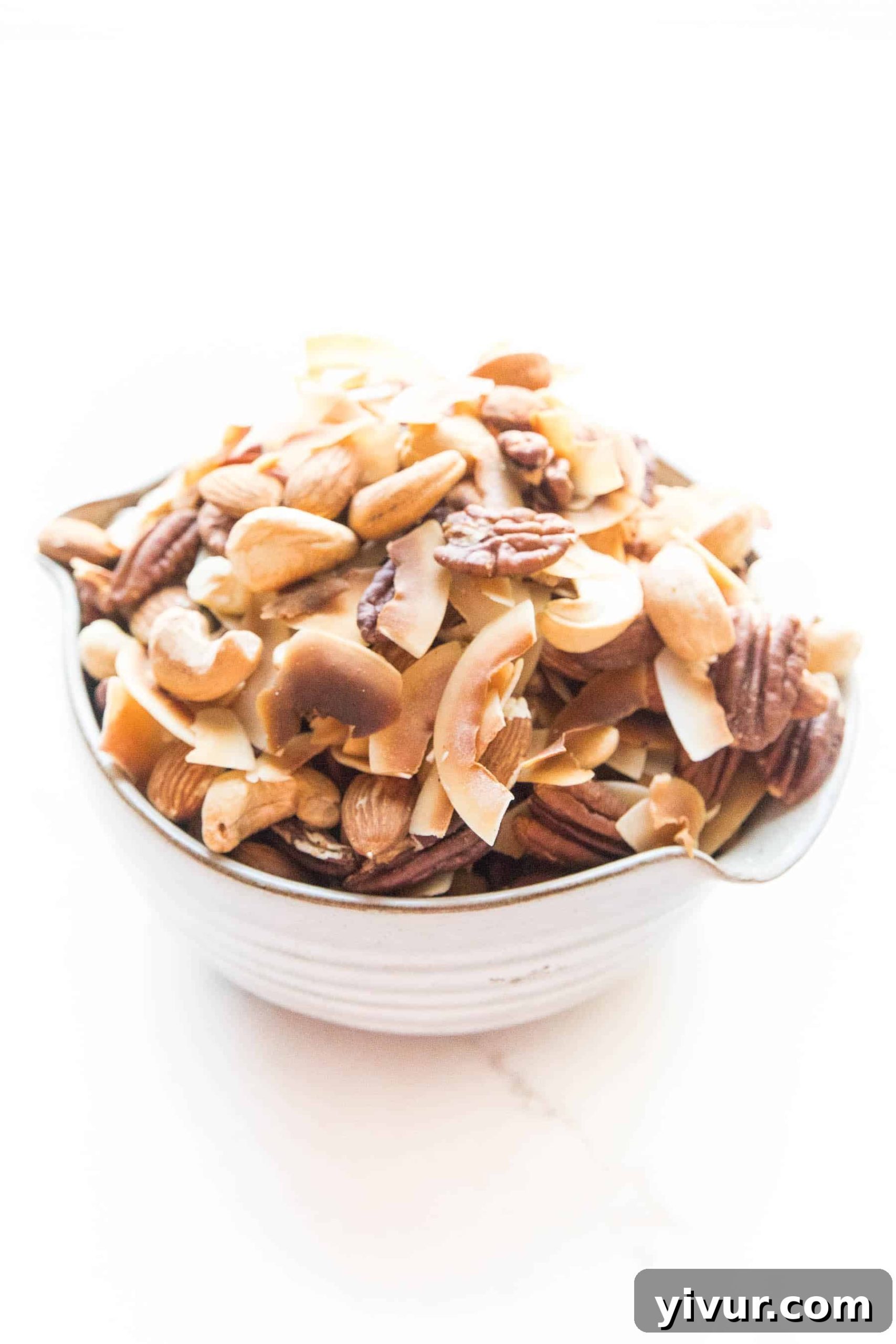A close-up view of the perfectly roasted Whole30 and Keto nuts and coconut chips trail mix in a pristine white bowl, emphasizing texture and color.