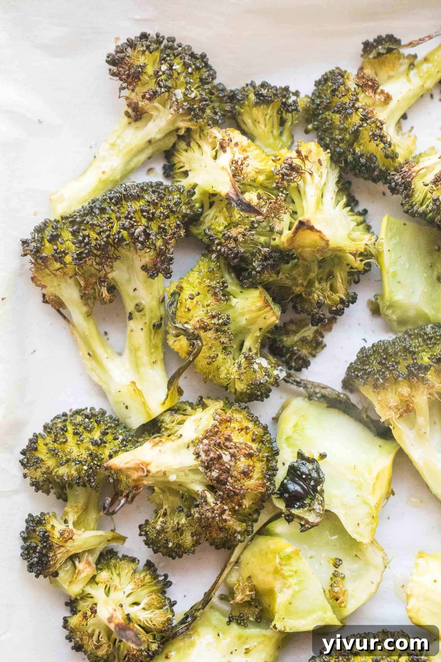 Close-up of golden-brown roasted broccoli on a parchment-lined baking sheet.