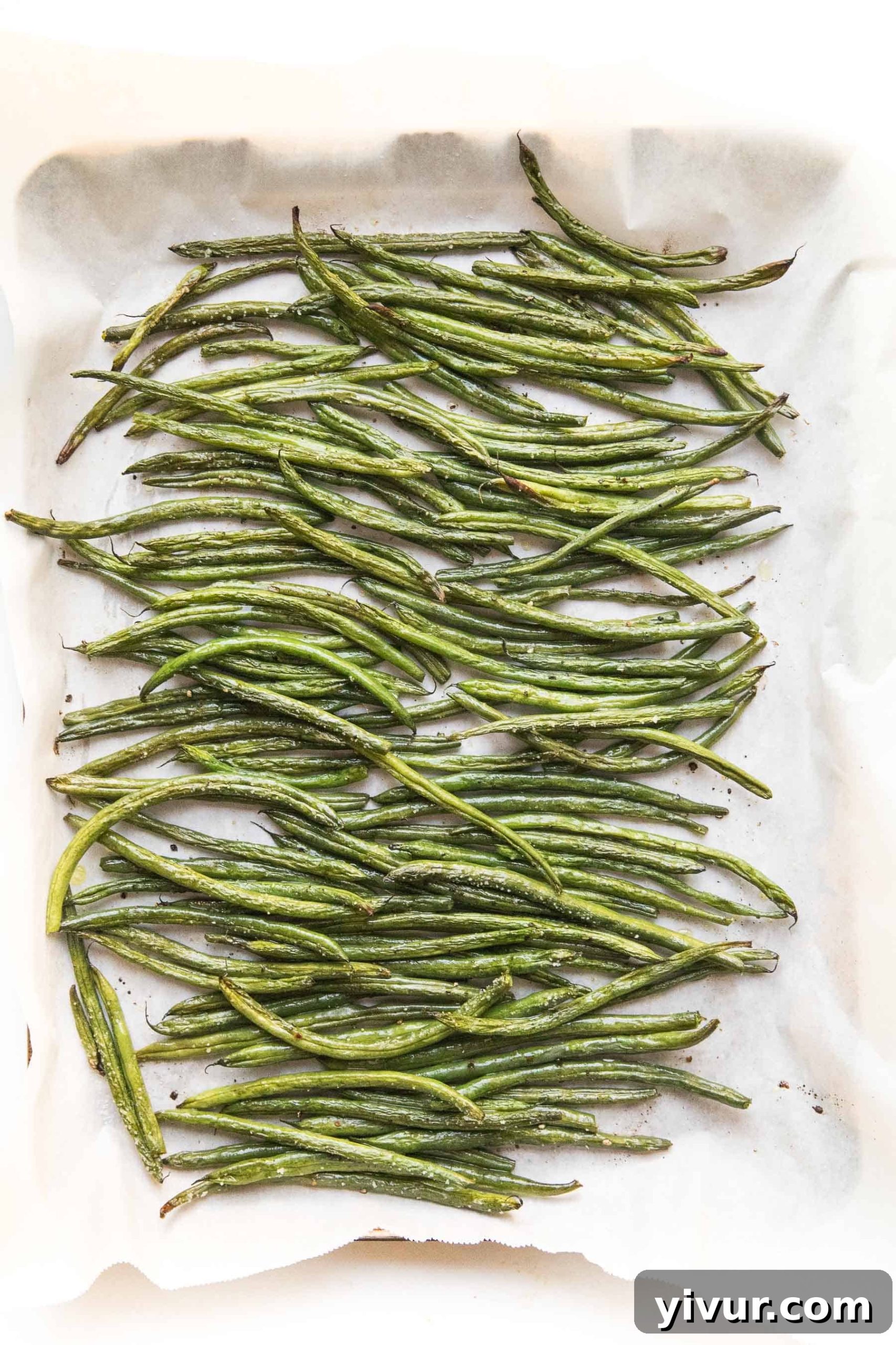 Crispy roasted green beans spread on a rimmed baking sheet