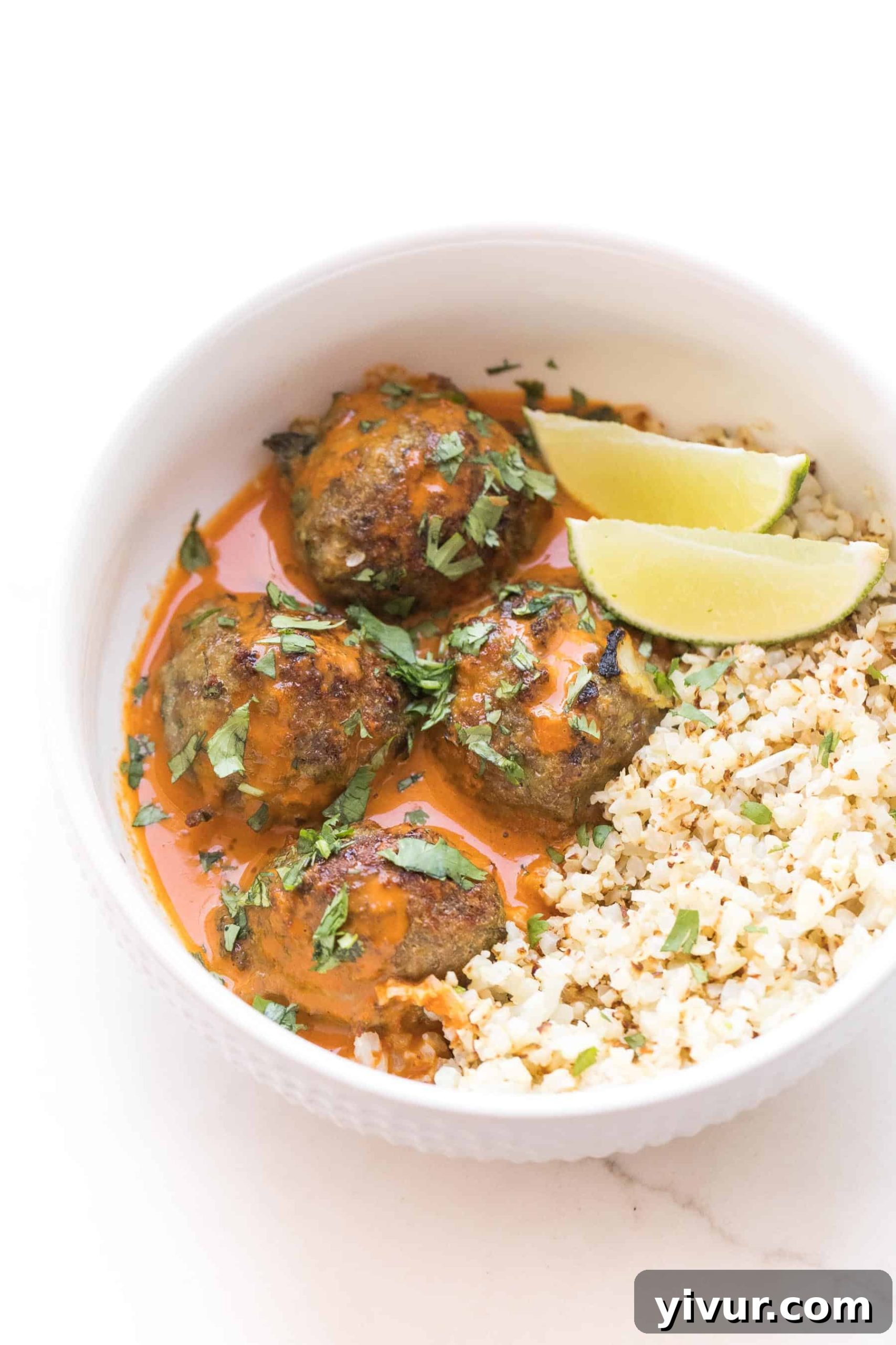 Juicy Thai Curry Meatballs in a white bowl with a rich, creamy sauce, garnished with fresh cilantro and lime.