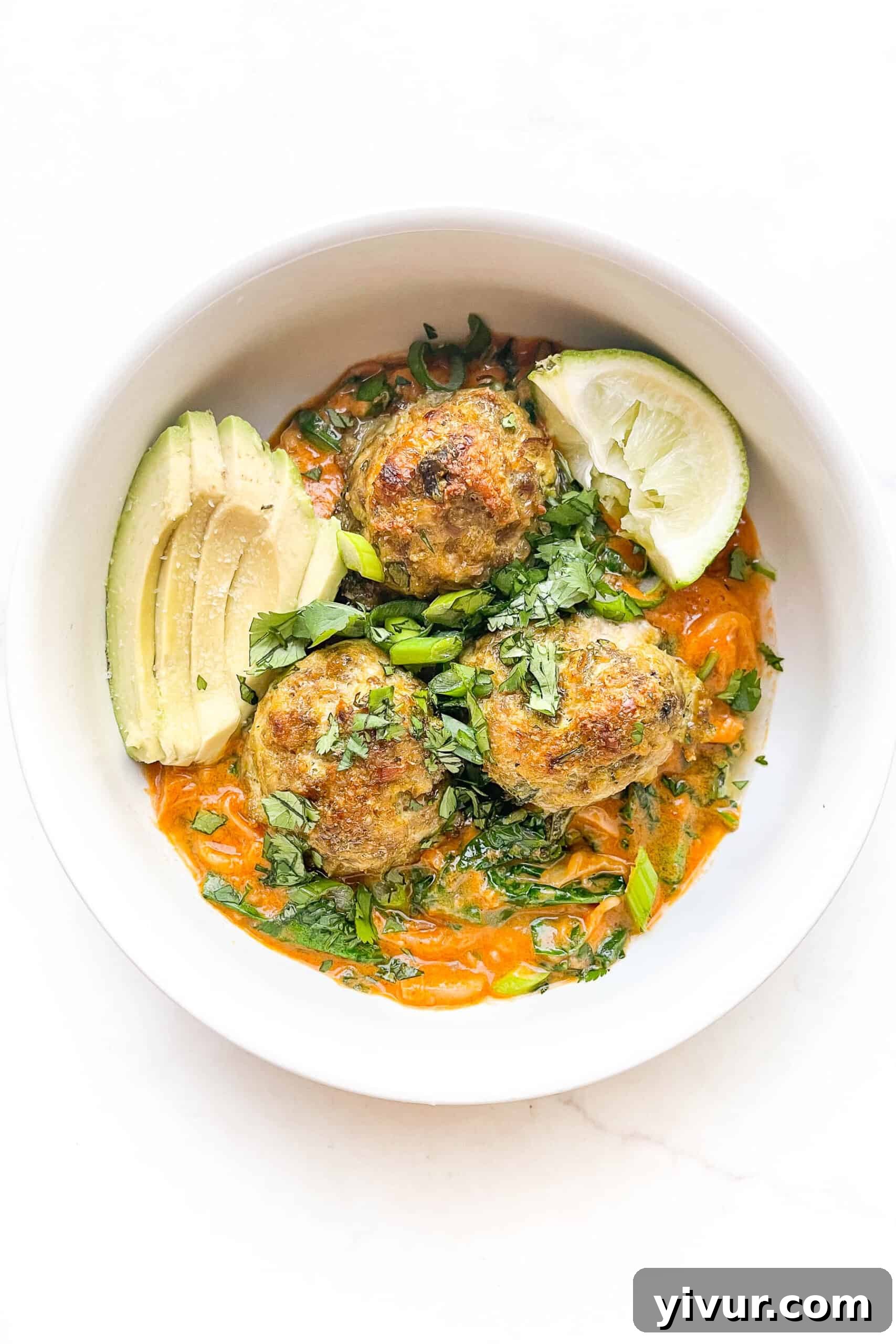 Thai curry meatballs served over noodles and curry sauce in a white bowl, garnished with fresh cilantro and lime.