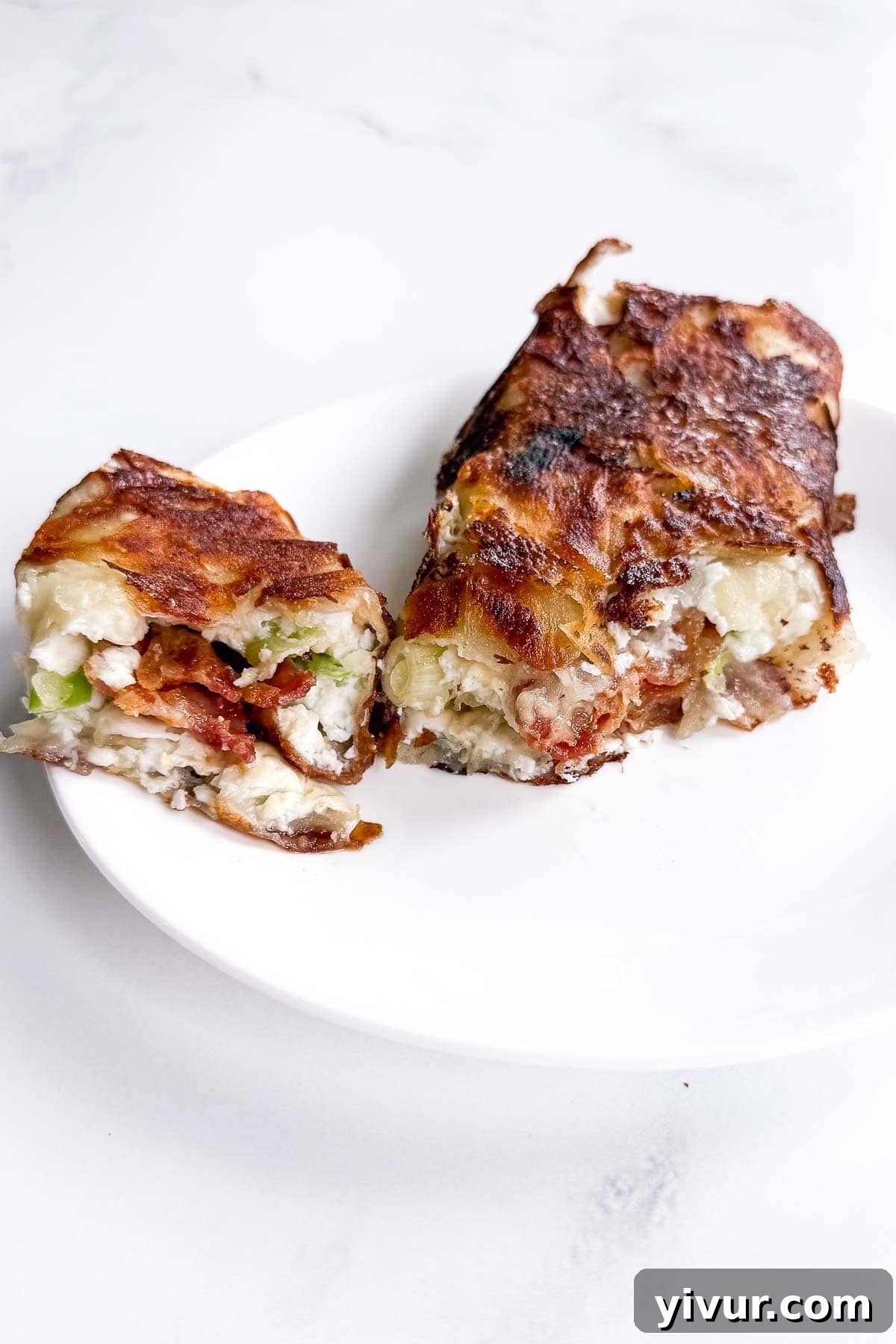 Two pieces of a crispy, golden-brown breakfast burrito filled with eggs, bacon, potatoes, and green onions are served on a white plate, ready to energize your morning.