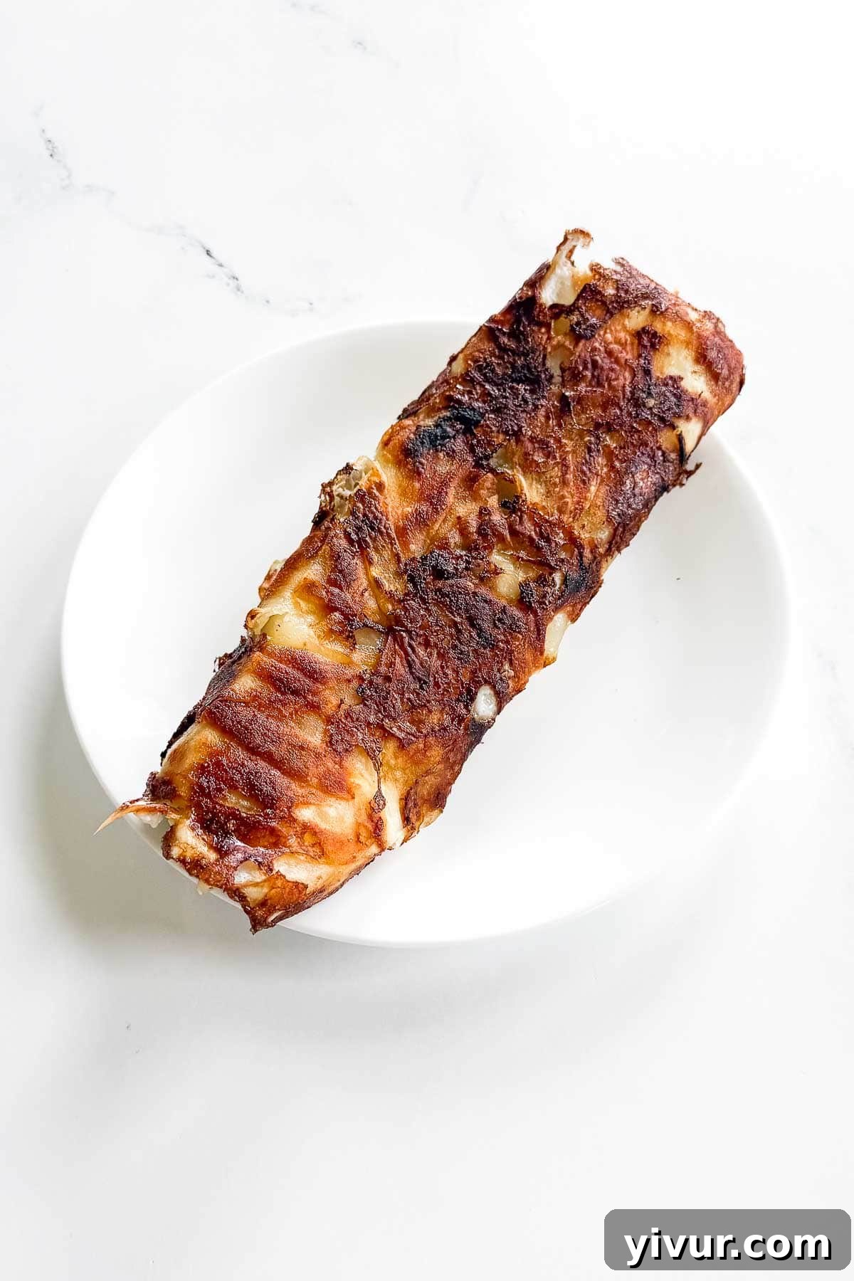 A rectangular piece of crispy, browned potato breakfast burrito sits on a white plate, ready to be enjoyed.