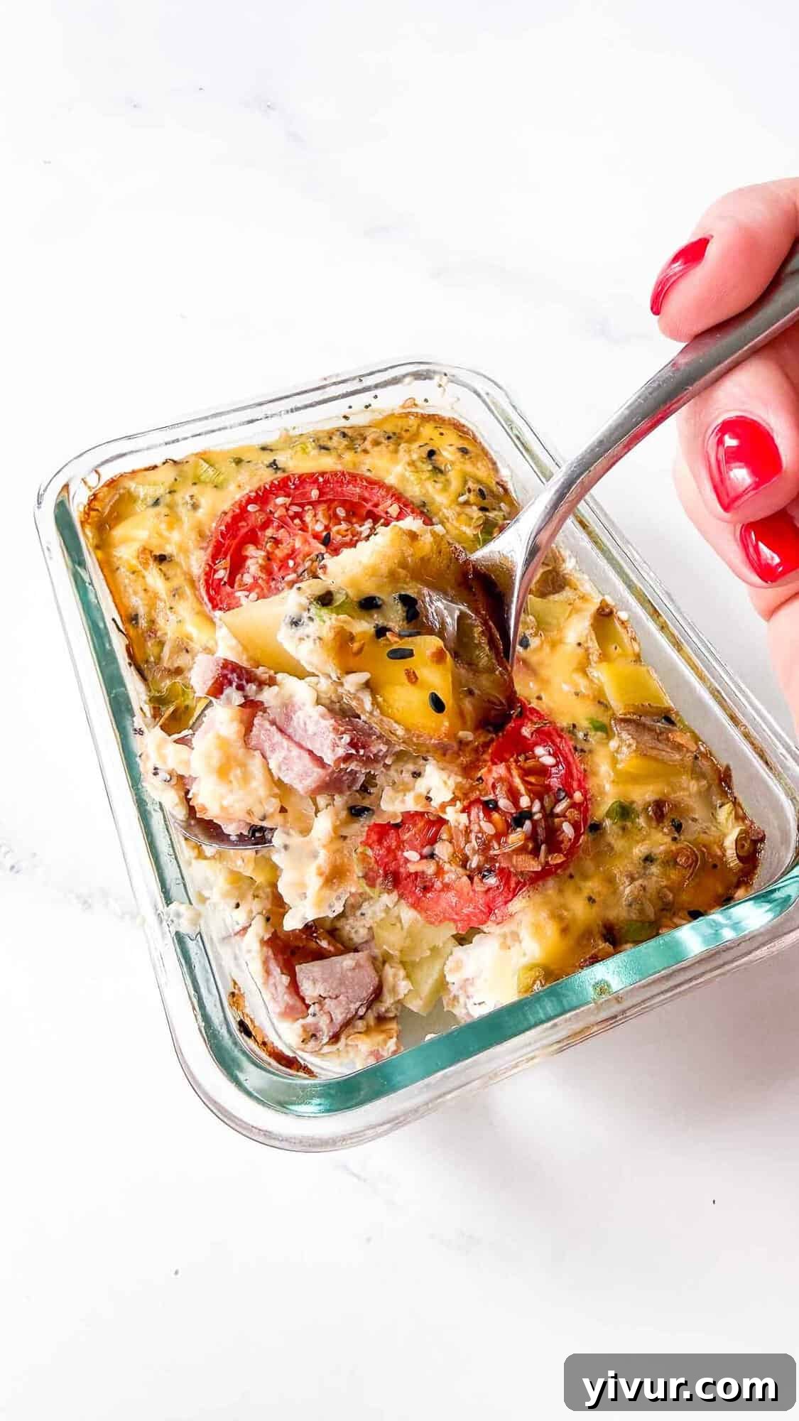 High-Protein Ham, Egg & Potato Meal Prep Bowls for Busy Days 2 Natalie’s hand with red-painted nails lifts a forkful from a glass dish of baked egg casserole topped with tomato, sausage, and herbs—perfect for sharing on your WordPress blog using a Custom Post Template.
