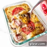 High-Protein Ham, Egg & Potato Meal Prep Bowls for Busy Days 7 A hand with red nail polish holds a fork lifting a bite of high protein baked casserole with tomatoes, sausage, potatoes, eggs, and herbs—perfect for meal prep—in a glass dish on a white surface.