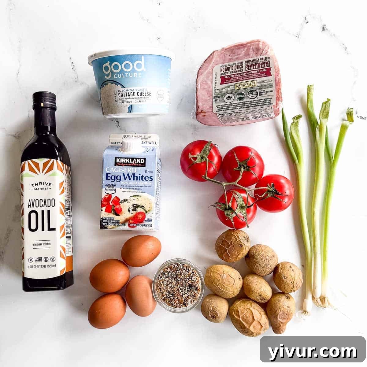 High-Protein Ham, Egg & Potato Meal Prep Bowls for Busy Days 3 A bottle of avocado oil, egg whites, cottage cheese, a ham slice, tomatoes on the vine, green onions, brown eggs, and small potatoes make the perfect high protein Ham Egg and Potato meal prep on a white surface.